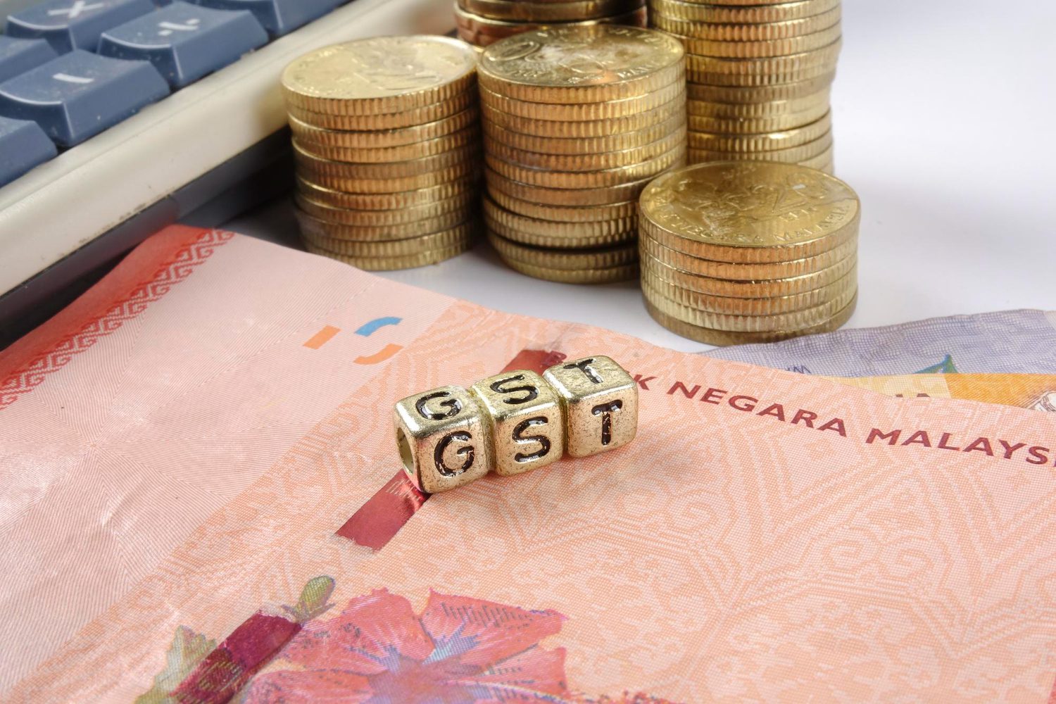 close up of gst letter blocks with stacked coins and paper currency by calculator against gray background